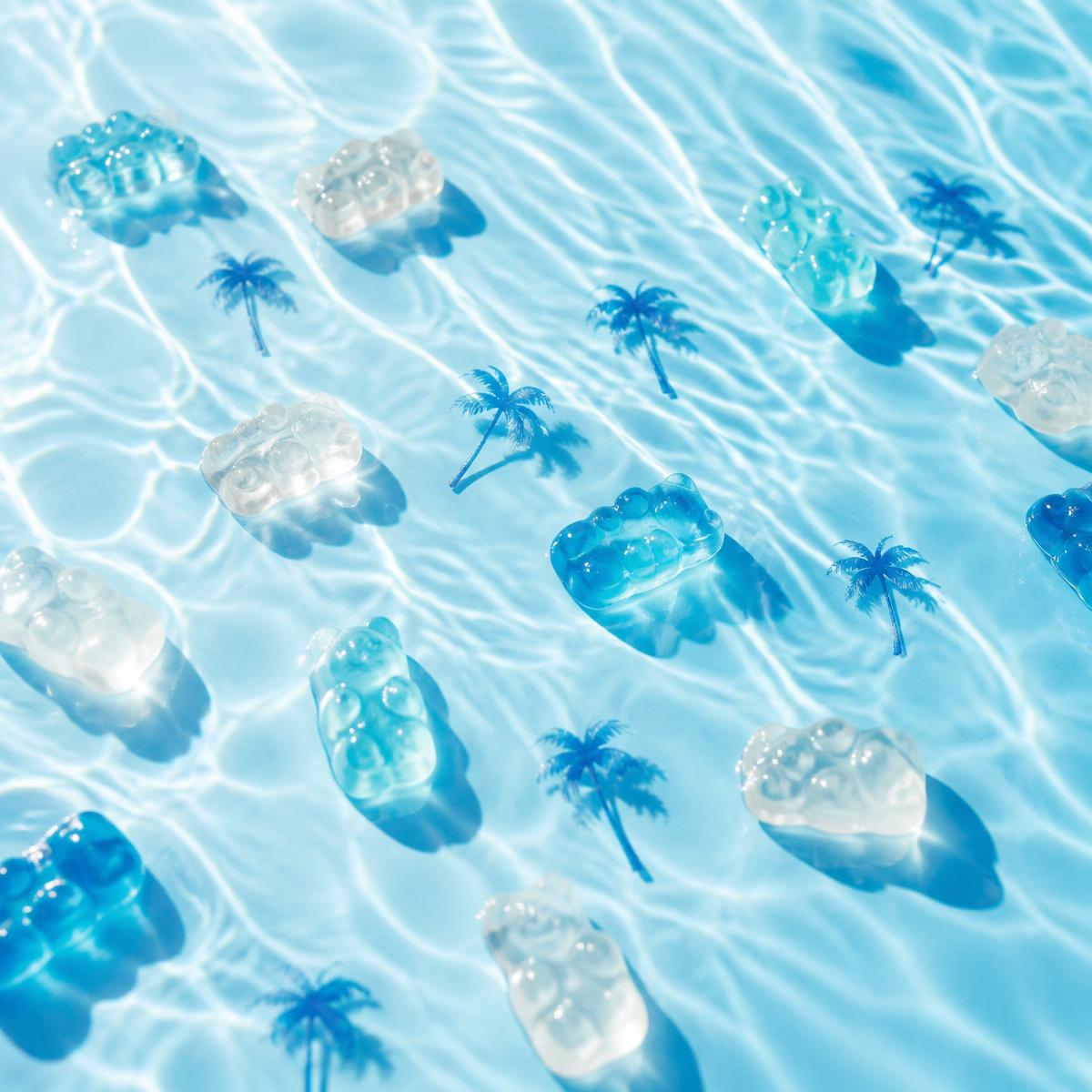 Translucent blue gummies floating on sparkling pool water with palm tree silhouettes